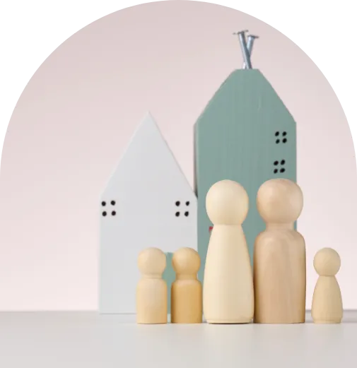Symbolische Darstellung des methodischen Familienstellens: Holzfiguren in verschiedenen Größen stehen vor stilisierten Häusern in sanften Farben.